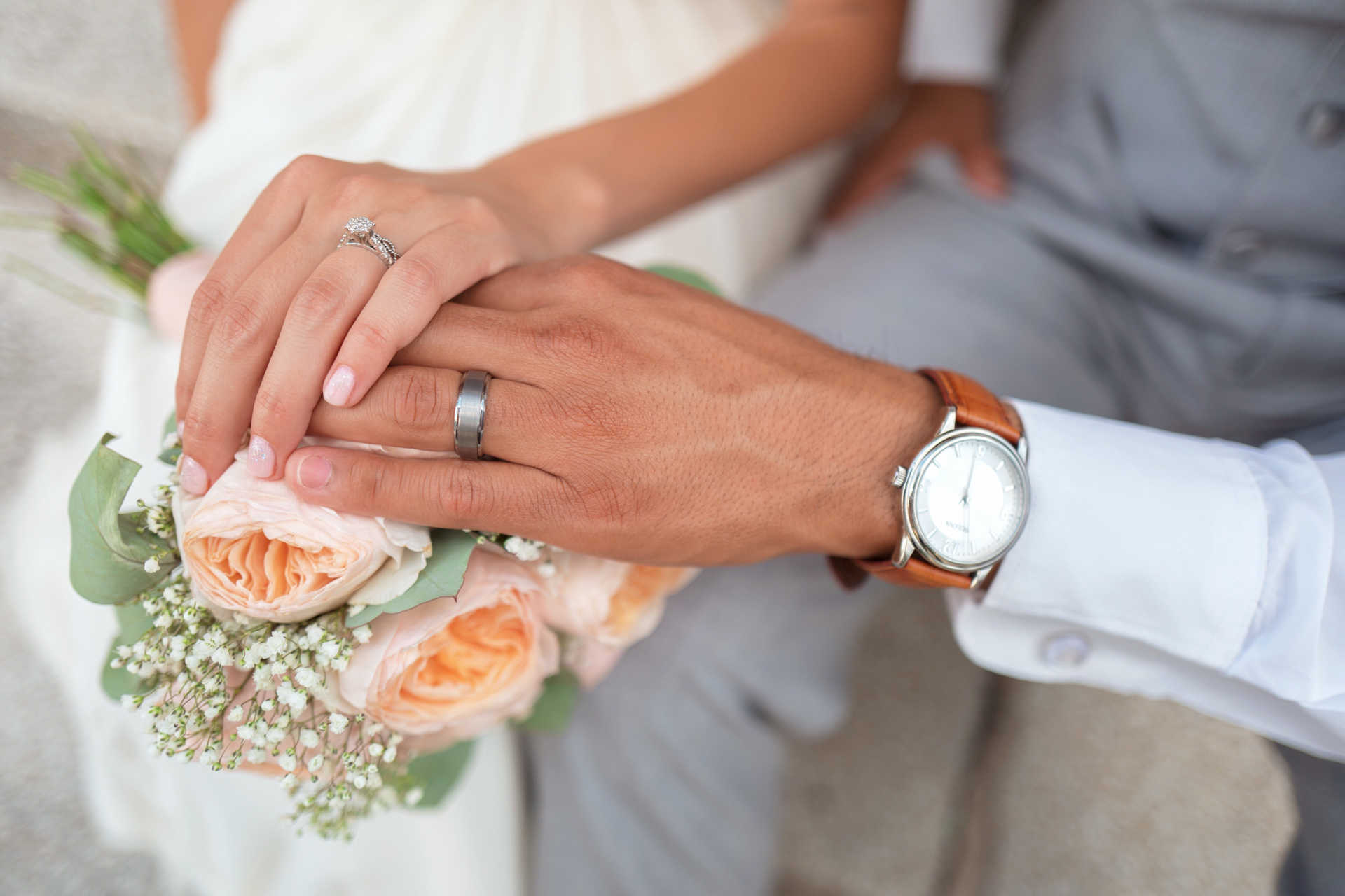 Brautpaar mit Ringen an den Fingern legen die Hände auf den Brautstrauß